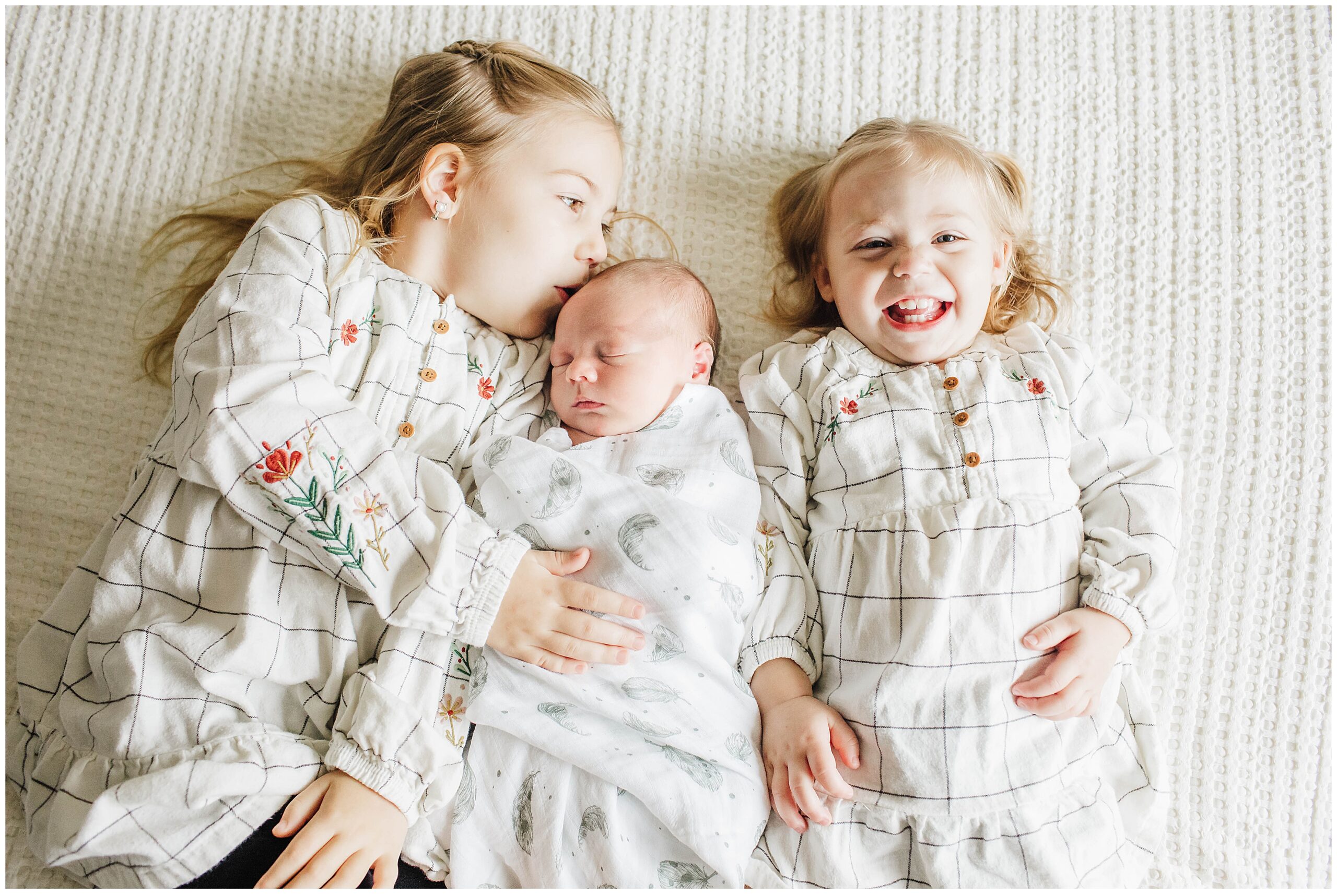 Image of siblings kissing baby brother during a newborn photoshoot